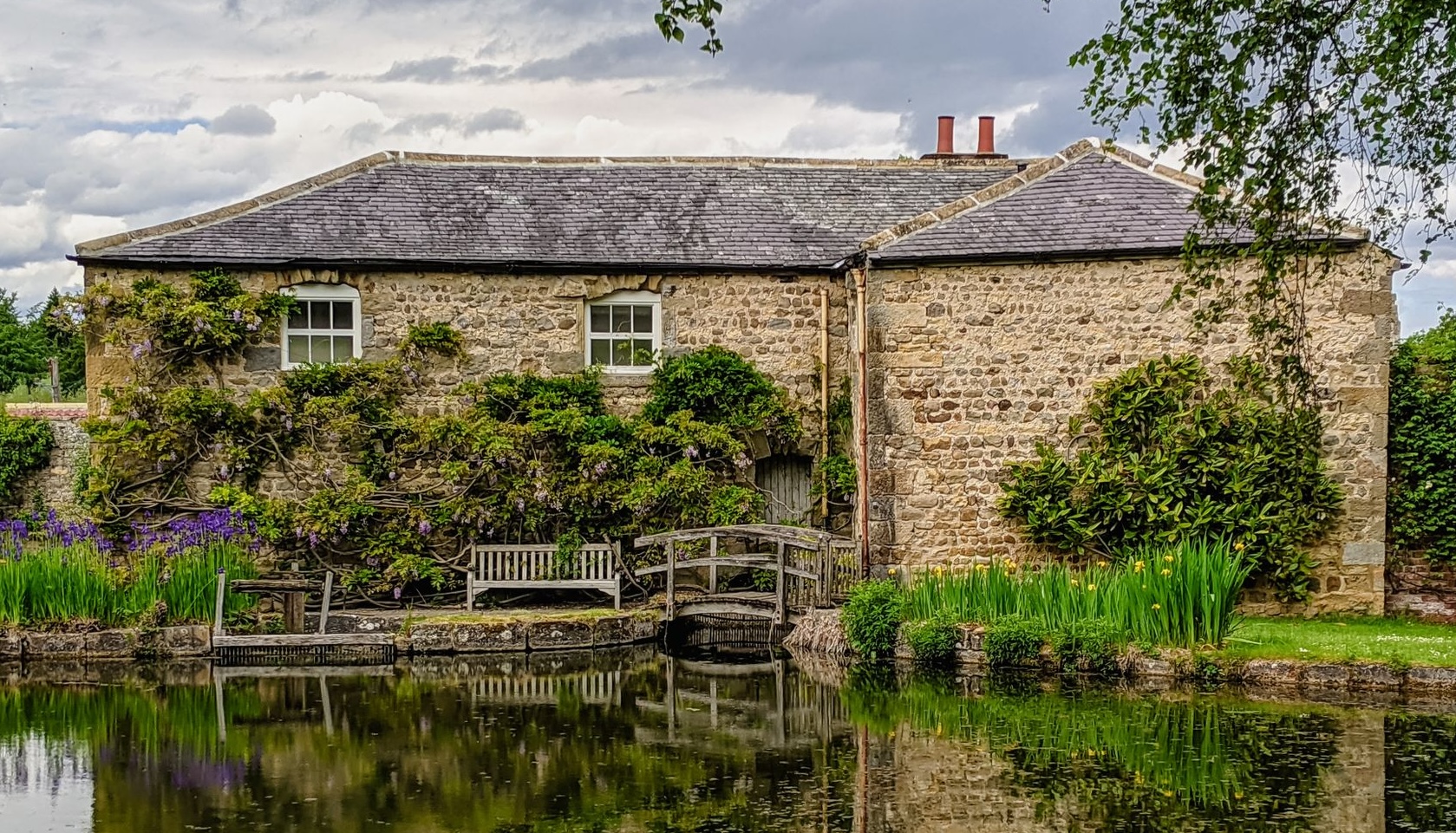 A serene view of a historic stone building reflected in a calm pond in North Stainley, England.