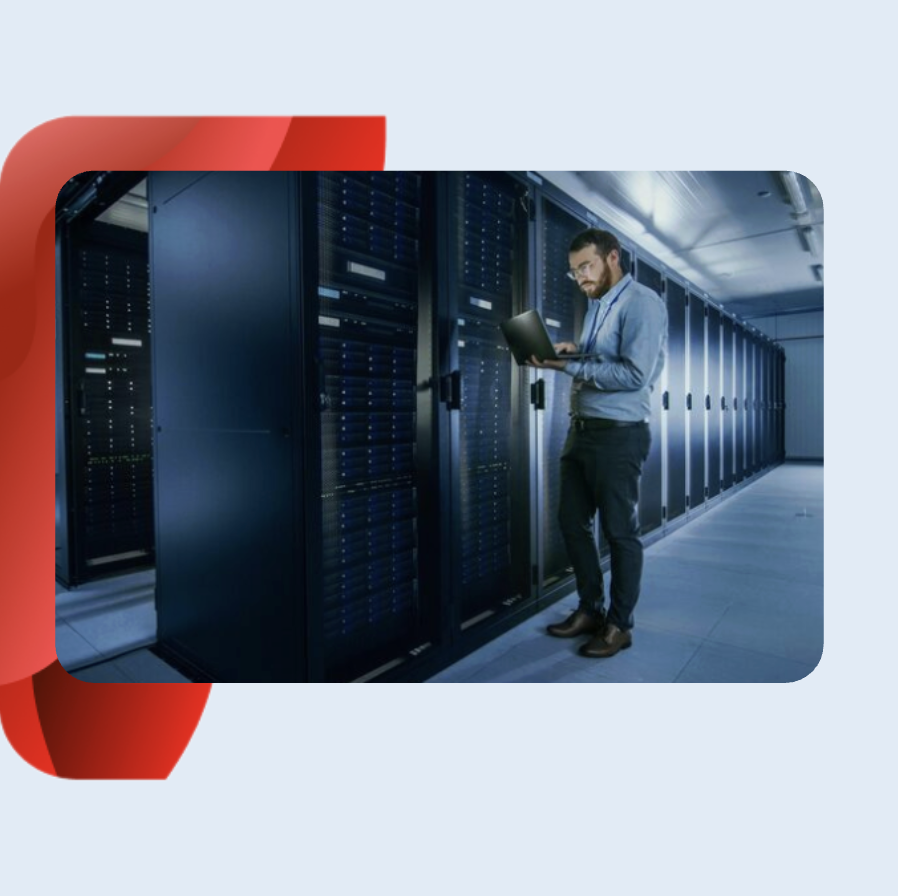 Man in business casual attire standing in a server room while looking at a laptop