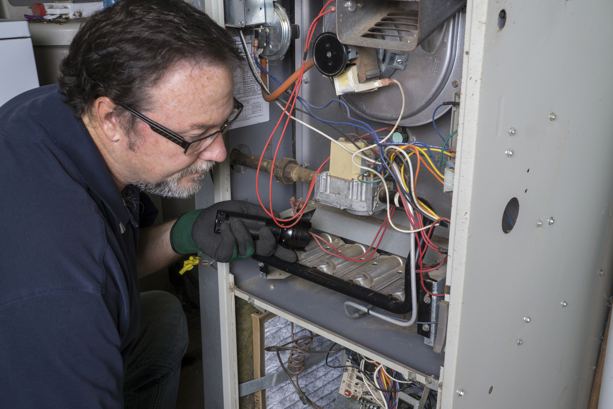 Man in glasses and gloves inspecting the wiring of an open furnace.