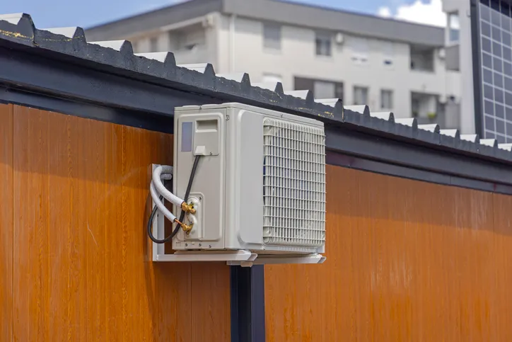 A white mini-split air conditioner condenser unit is mounted on the exterior wall of a building.