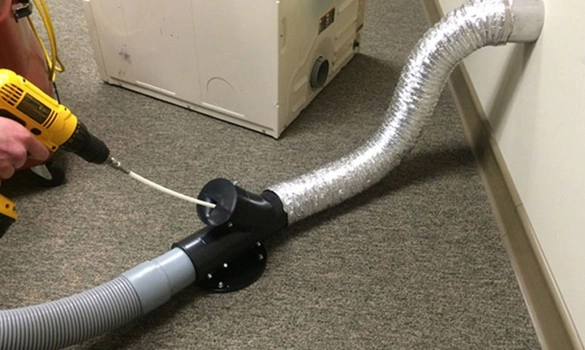 Person cleaning a dryer vent with a drill-powered brush.
