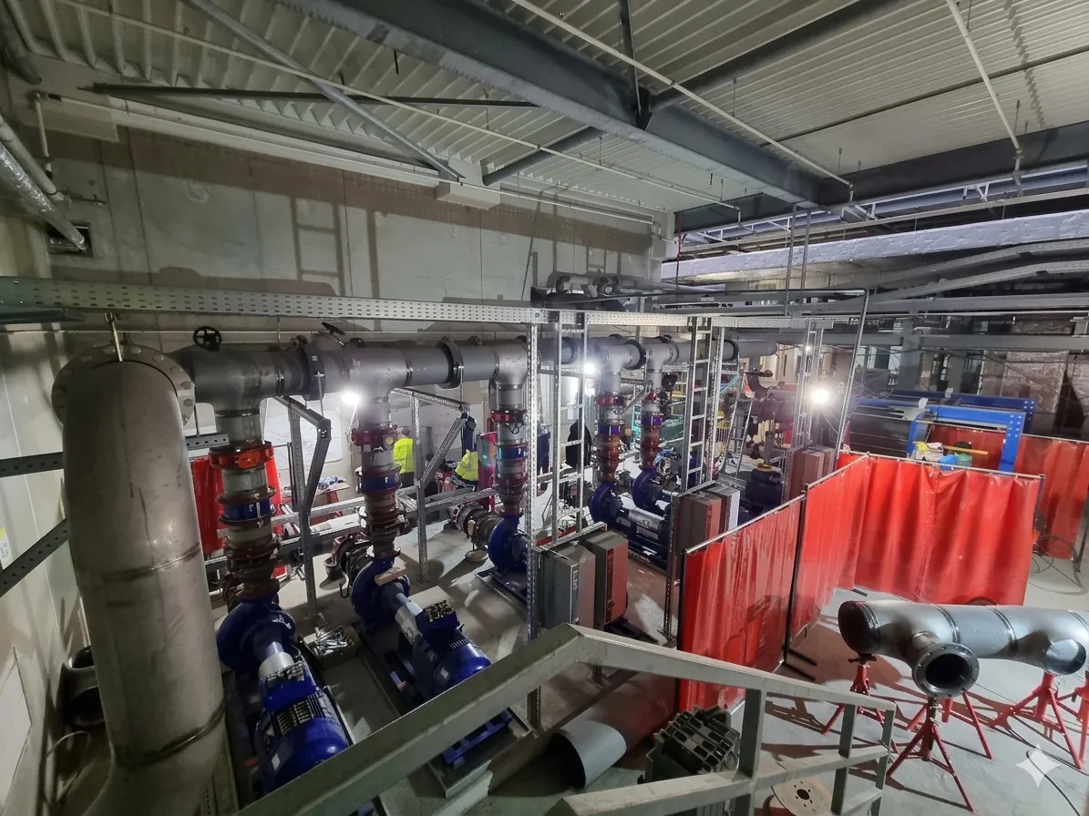 Montage einer industriellen Pumpstation und Stahlrohrleitungen in einer im Bau befindlichen Halle