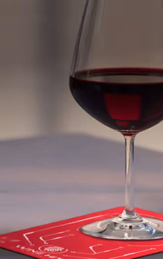 Glass of red wine on a red coaster with white circuit-like design and the word 'WINE HIT'.
