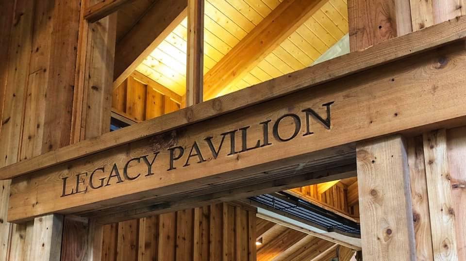 The top of an entry way to a building made out of wood. Above the entry way are the words "Legacy Pavilion" written into the wooden frame.