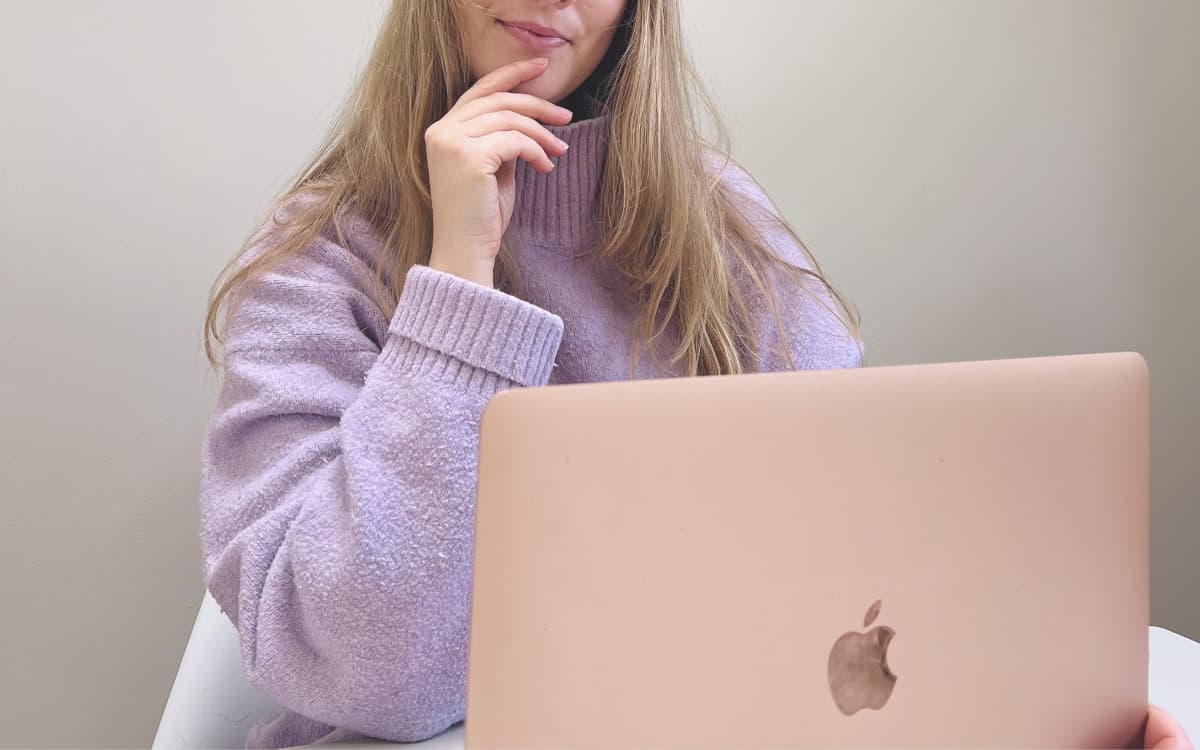woman in purple jumper pondering while looking at a laptop