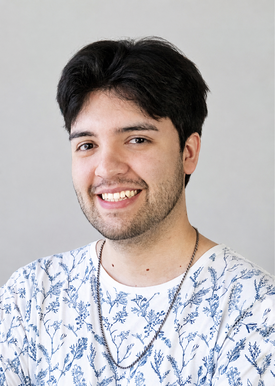 Smiling young man with dark hair wearing a white shirt with blue floral patterns and a silver chain necklace.
