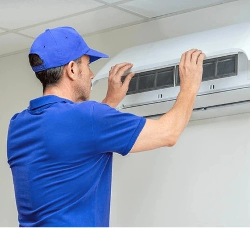 Technician in blue uniform checking and servicing wall-mounted air conditioner