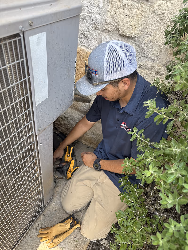 Technician in blue shirt working on outdoor utility equipment near plants