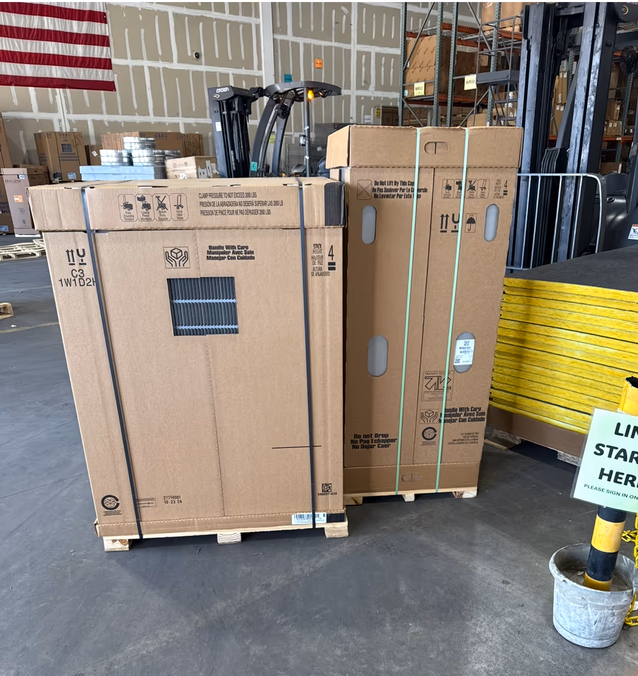 Large cardboard boxes strapped to pallets in warehouse with American flag