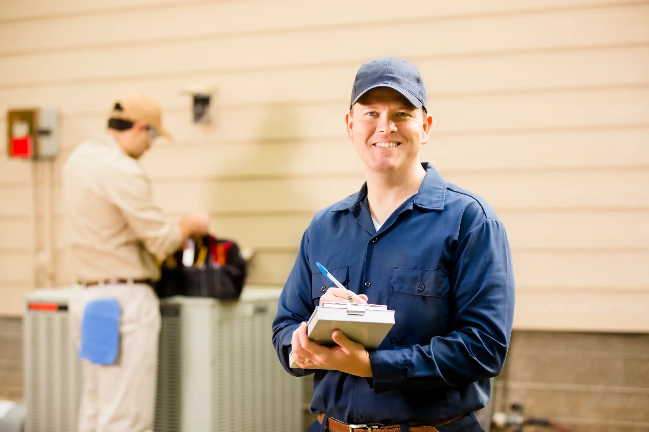 Smiling technician in blue uniform holding clipboard in workshop