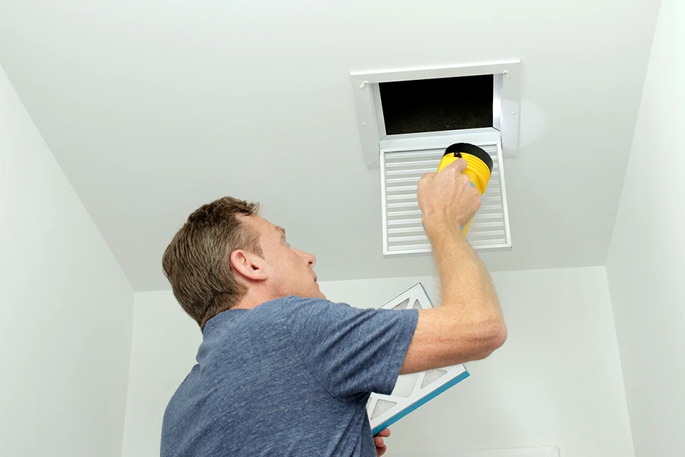 Person checking and cleaning ceiling air vent with yellow cloth