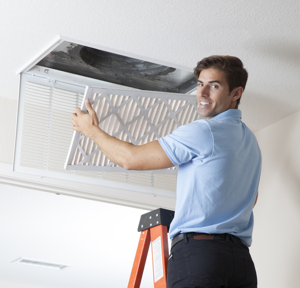 Technician replacing air filter in ceiling vent while standing on ladder