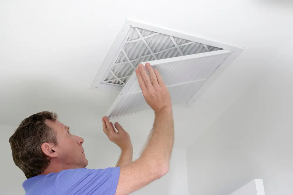 Person checking and removing air filter from ceiling vent