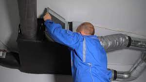 Worker in blue jacket inspecting ductwork near industrial ventilation system