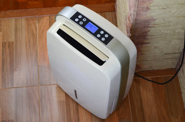 White dehumidifier with digital display on wooden floor near wall