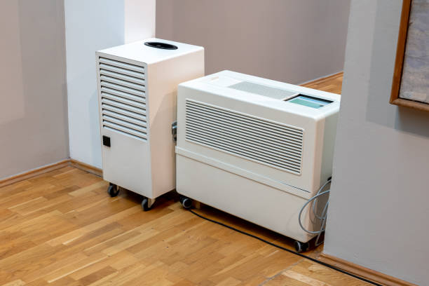 Two white dehumidifiers on wheels sitting on wooden floor near wall