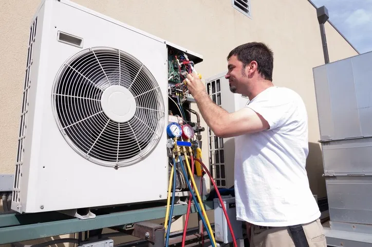 Technician checking and repairing an air conditioning unit outside a building