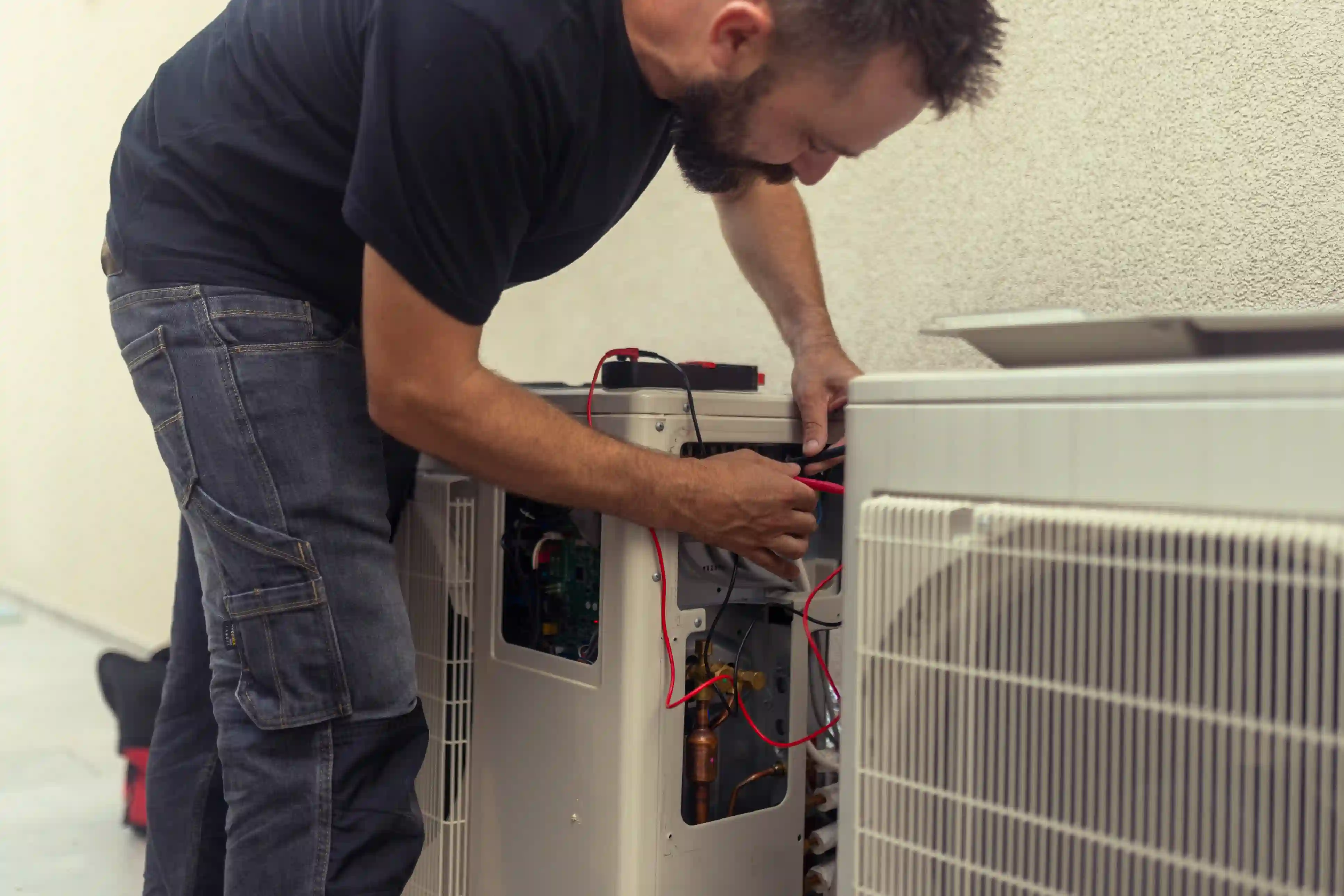 Technician repairing air conditioning unit with red electrical wires