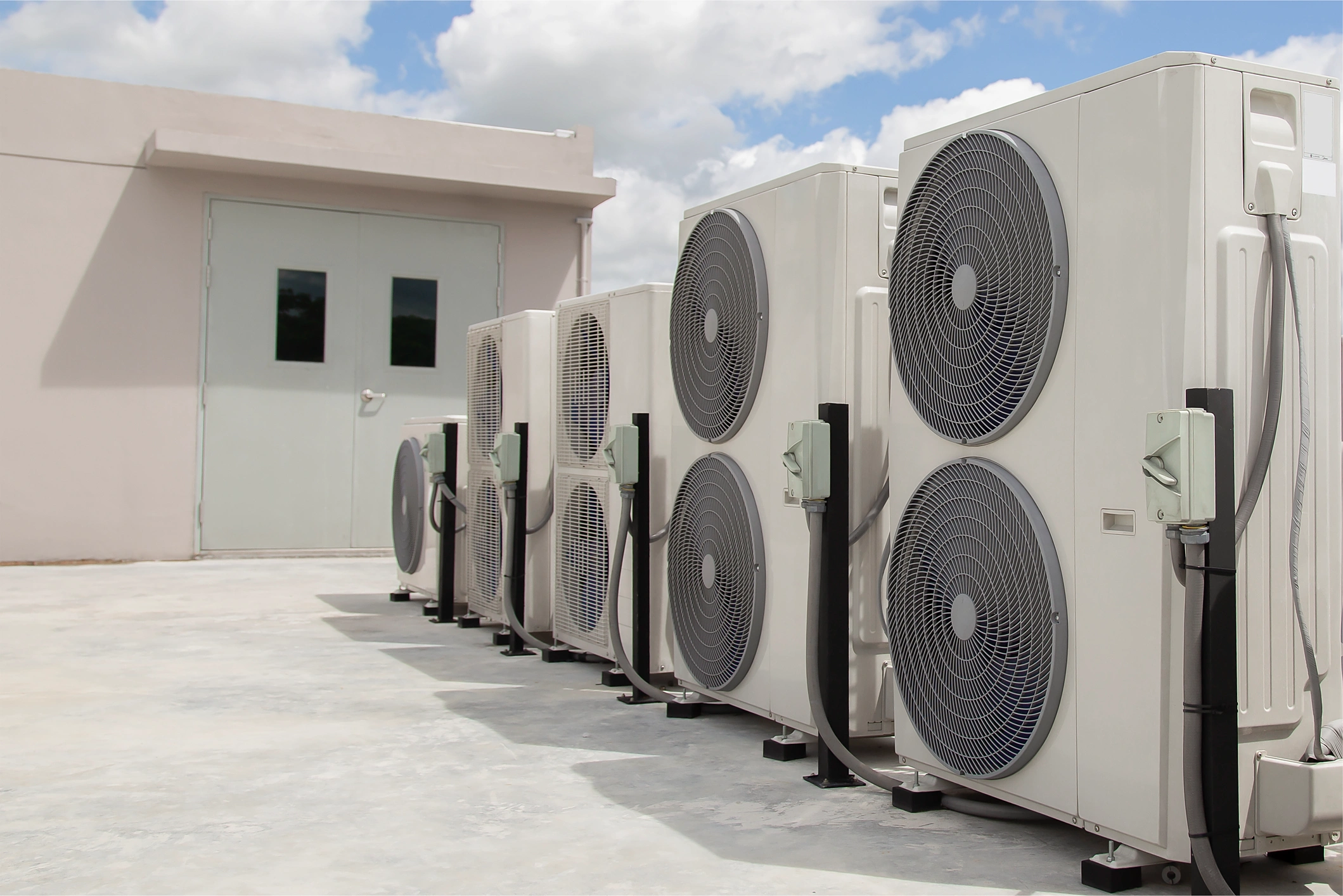 Multiple white air conditioning units lined up outside a building