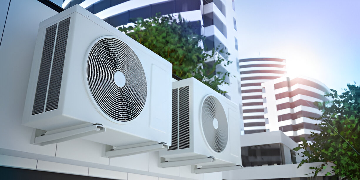 White air conditioning units mounted on building exterior with trees and sky