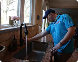 Plumber in blue shirt fixing kitchen sink near window with flowers