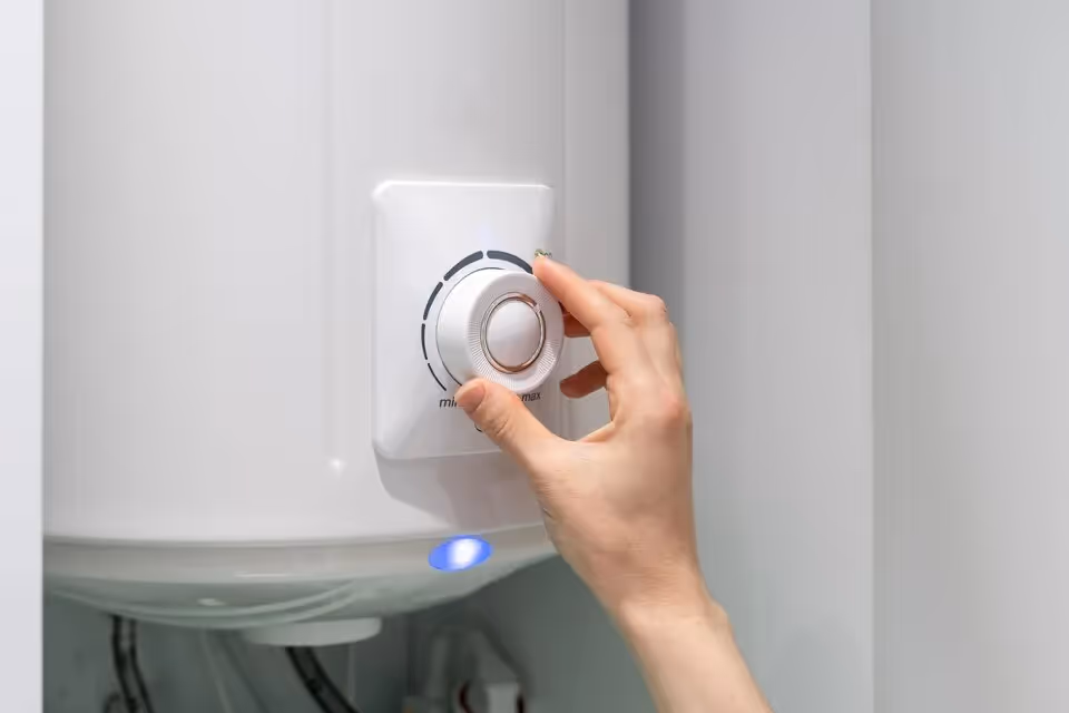 Hand adjusting temperature dial on white electric water heater