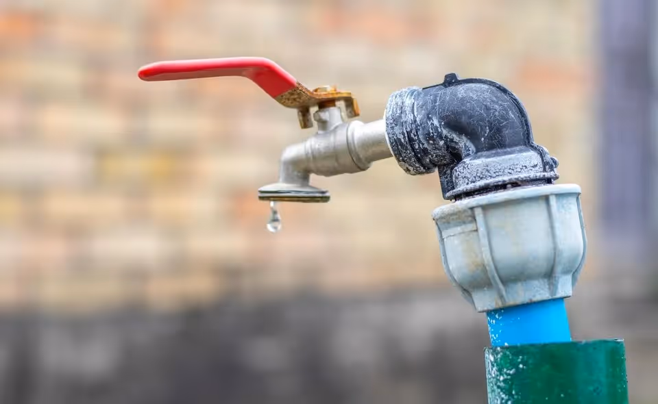 Water dripping from outdoor faucet with red handle and metal pipe