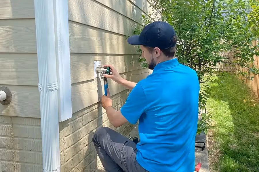 Person in blue shirt fixing outdoor plumbing near house wall