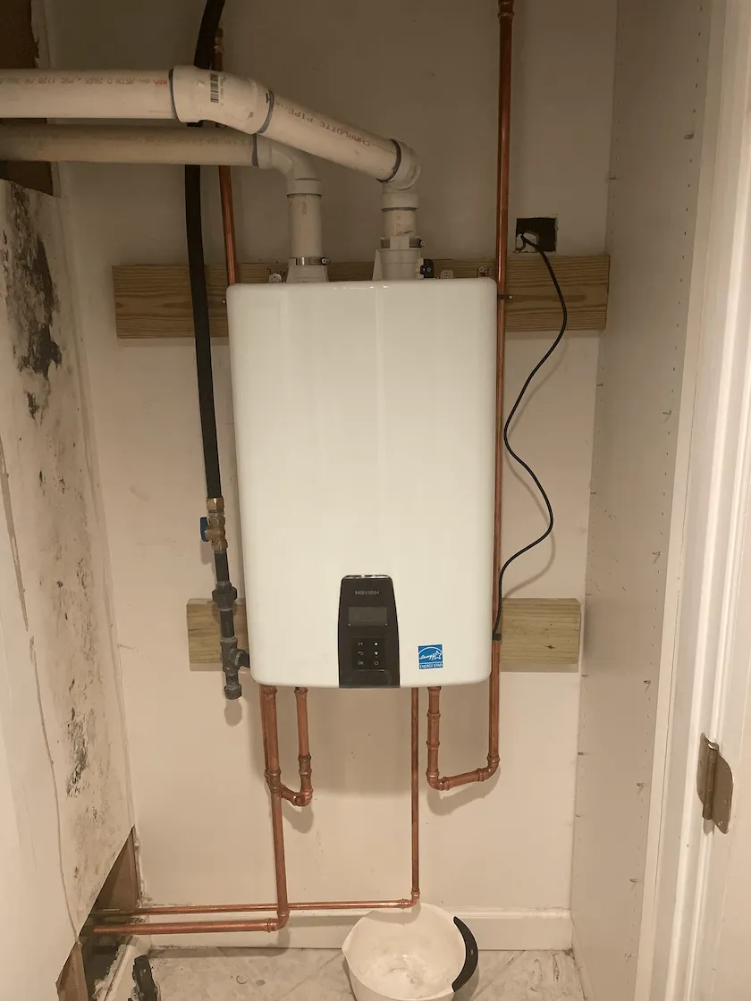 Tankless water heater mounted on wall with copper pipes and electrical connections