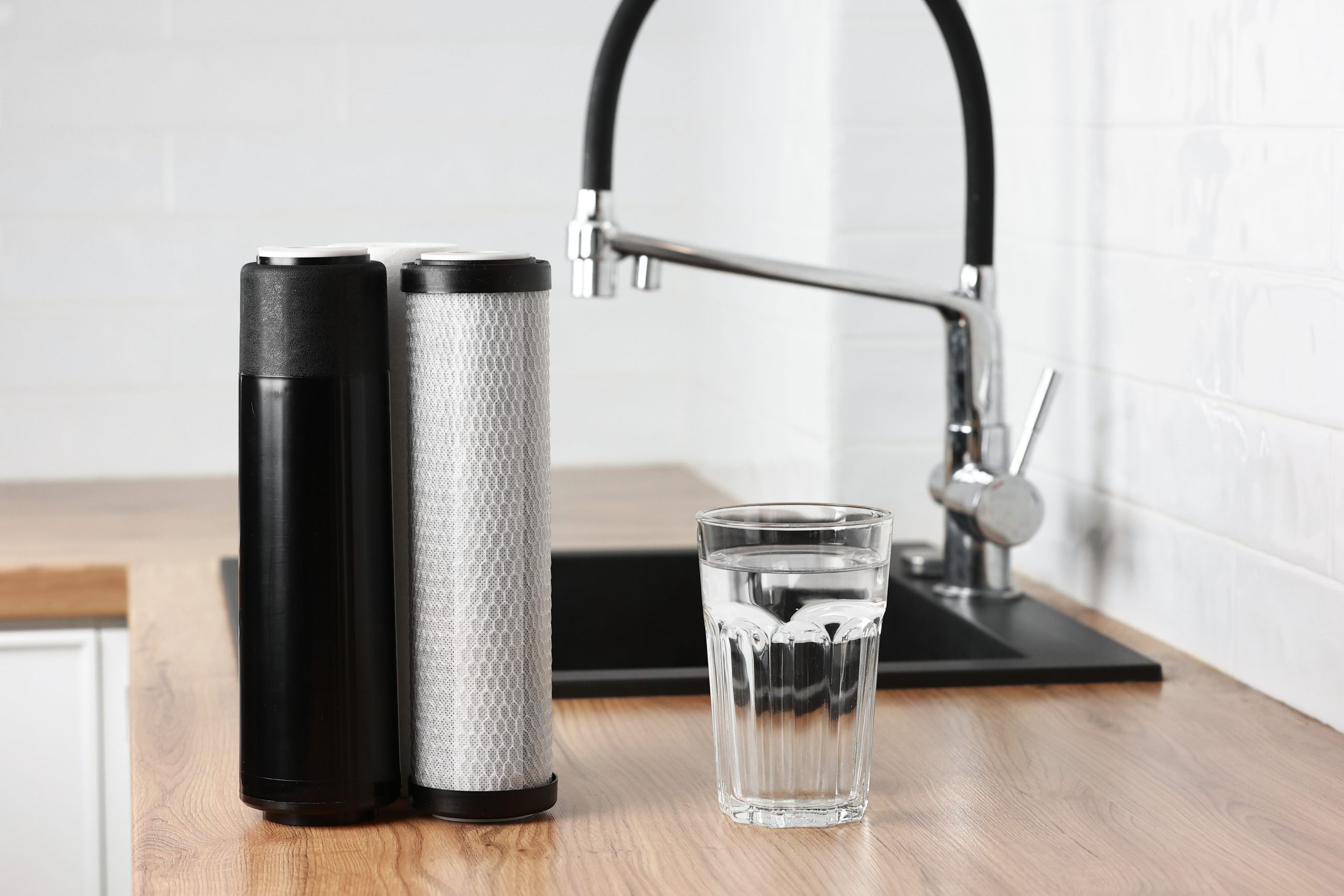 Water filter system with glass of clean water near modern kitchen faucet