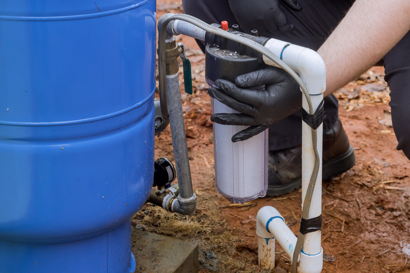 Hands in gloves installing water filter connected to blue water barrel