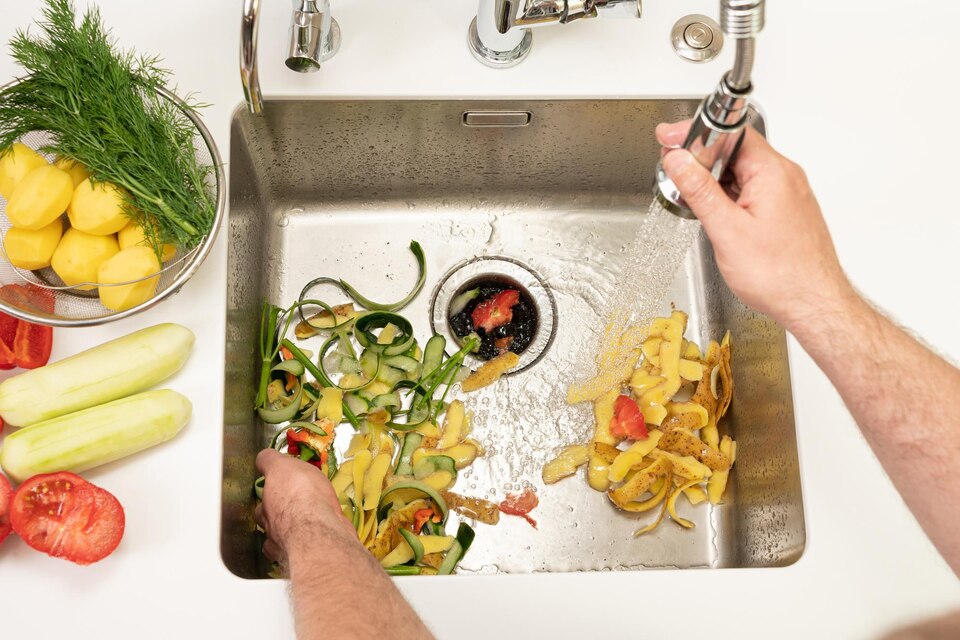 Hands washing vegetable scraps and peels in kitchen sink