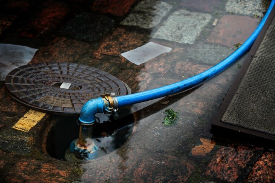 Blue water hose connected to urban street drain with textured pavement