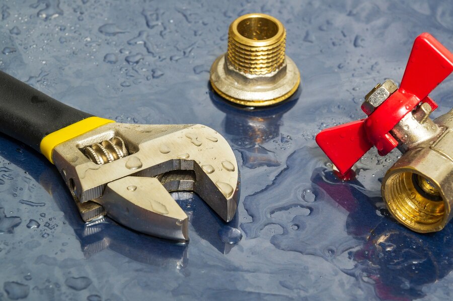 Plumbing tools and brass fittings with water droplets on blue background
