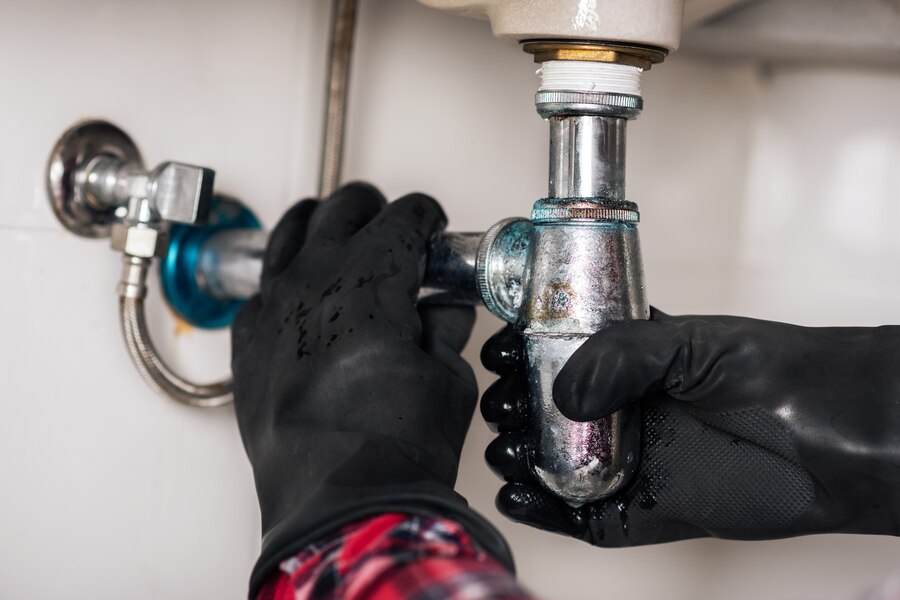 Hands in black gloves fixing a metal plumbing pipe connection