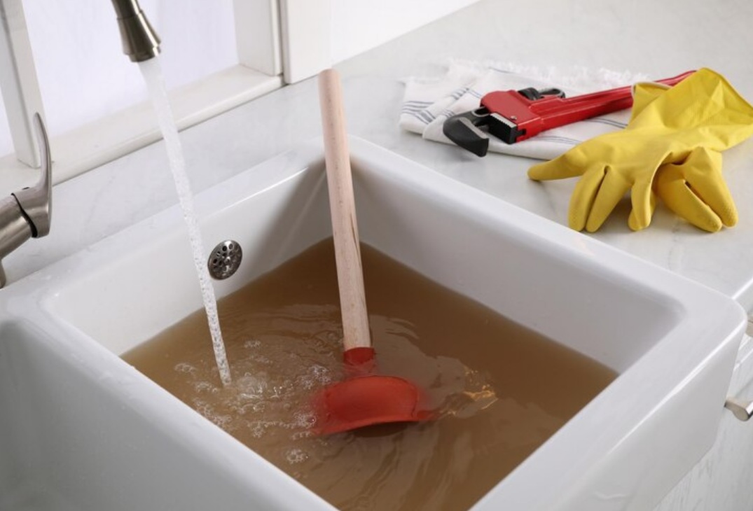 Clogged sink with plunger, running water, wrench, and yellow gloves