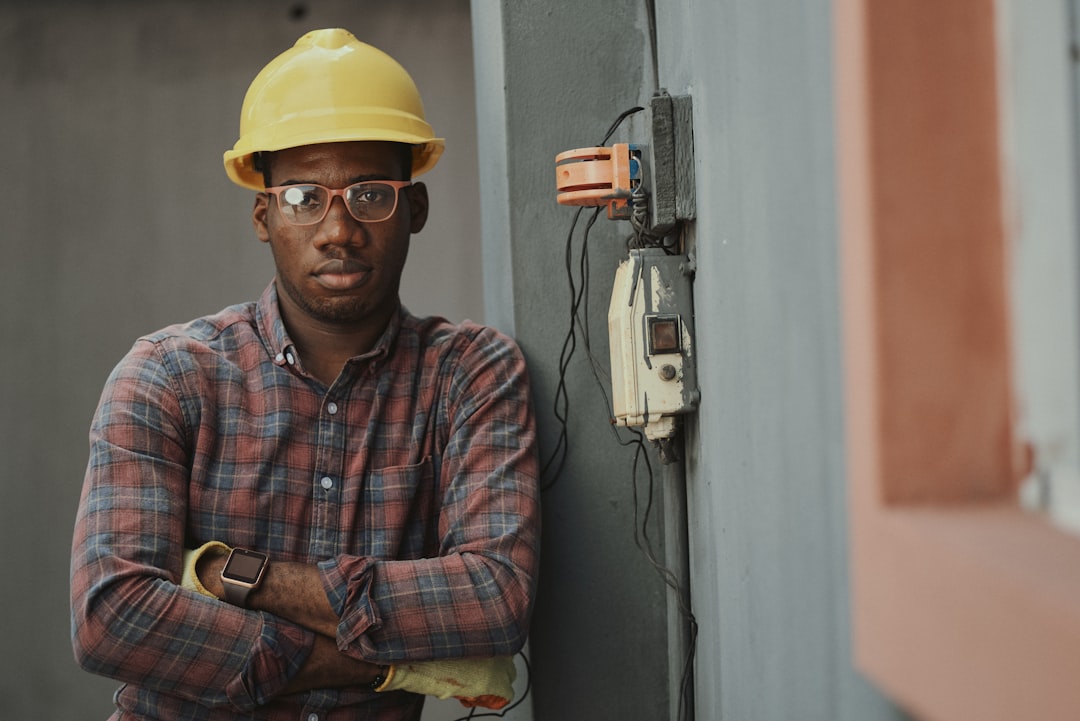Construction worker in hard hat and plaid shirt standing near electrical panel