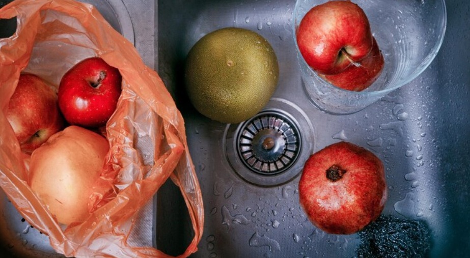 Colorful fruits in plastic bag and on wet kitchen sink with drain