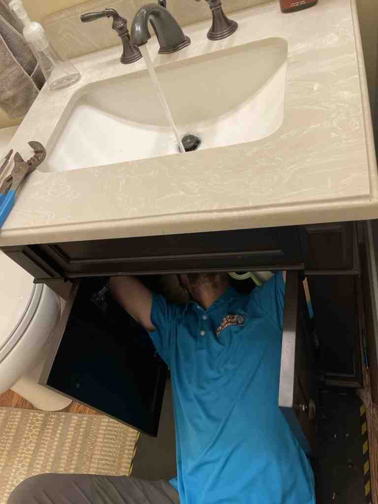 Person in blue shirt working under bathroom sink cabinet