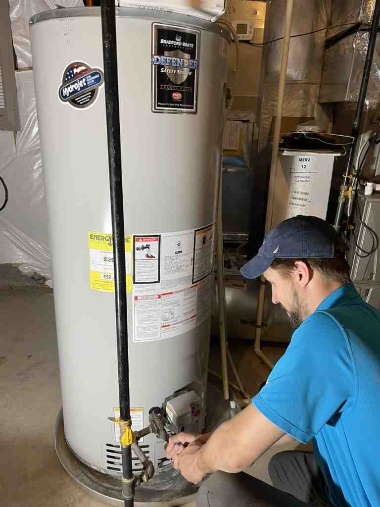 Technician in blue shirt repairing a white water heater in utility room