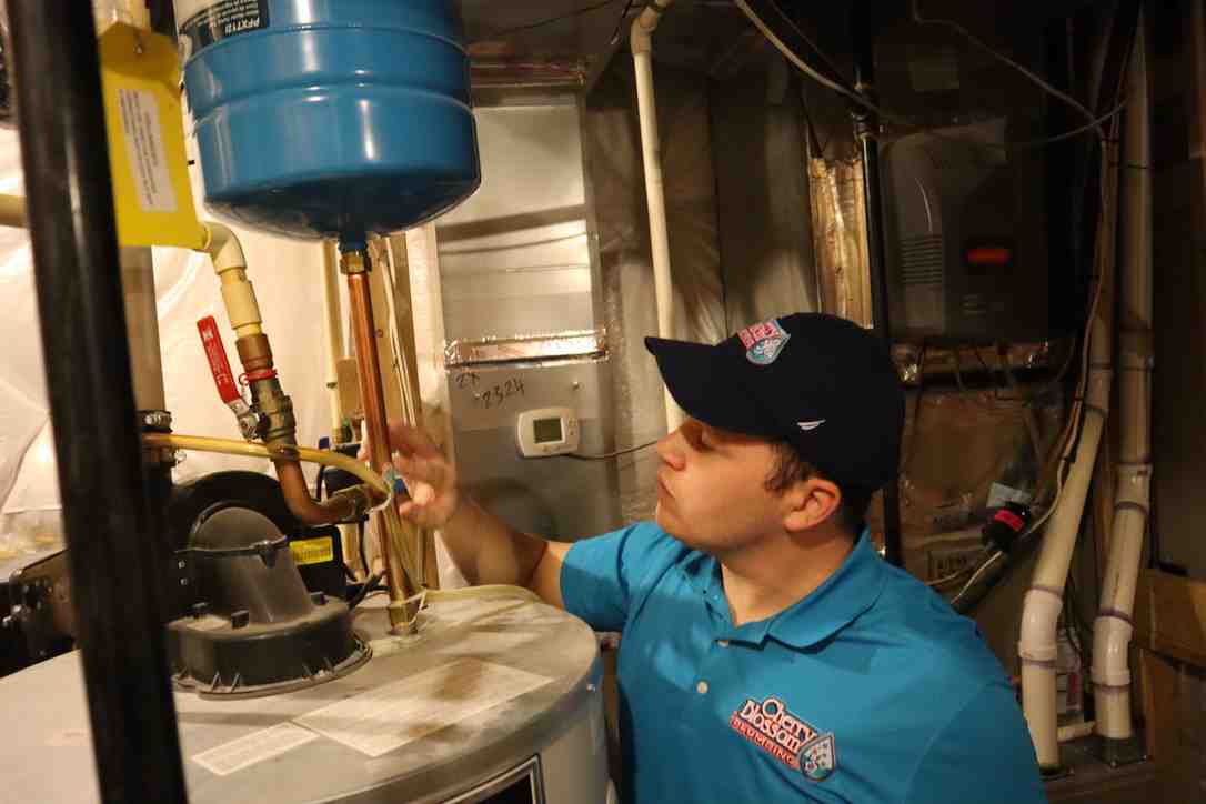 Technician in blue shirt checking water heater pipes in utility room