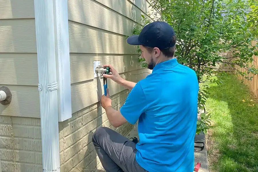 Technician in blue shirt repairs exterior wall fixture near green lawn