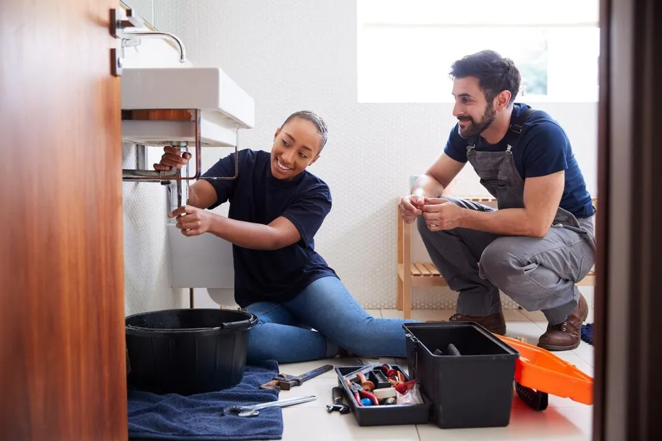 Plumbers working together to repair pipes under a bathroom sink