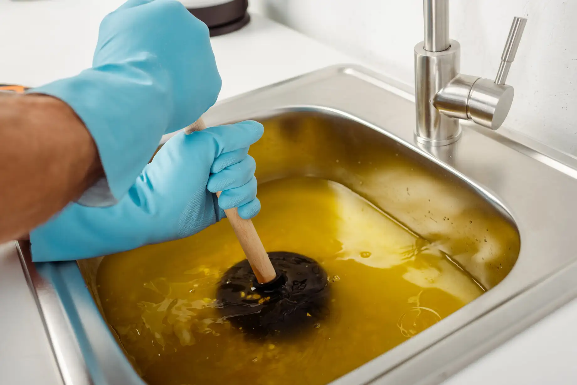 Gloved hand using plunger to unclog sink filled with yellow water