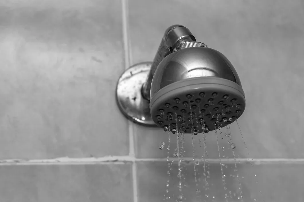 Metallic shower head with water droplets on tiled bathroom wall