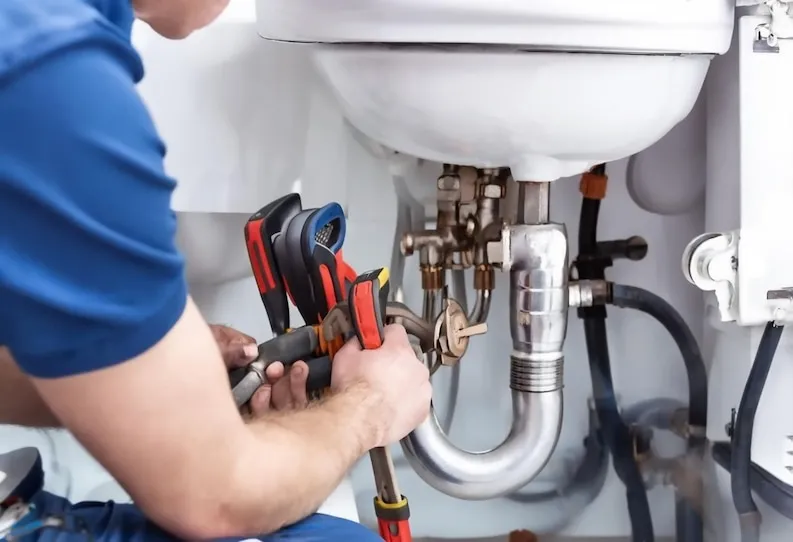 Plumber fixing pipes under sink with adjustable wrenches