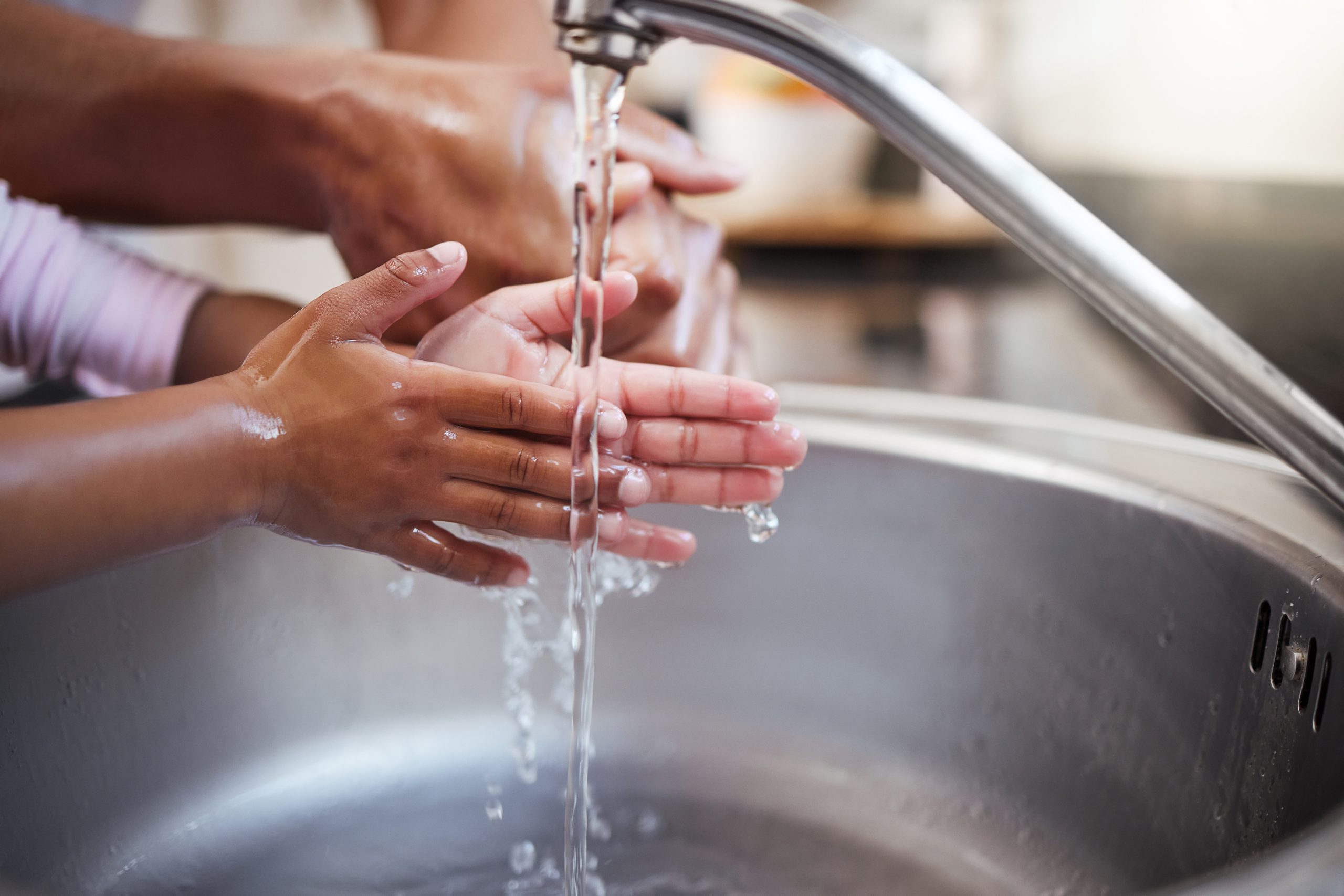 Hands being washed thoroughly under running water from a kitchen faucet