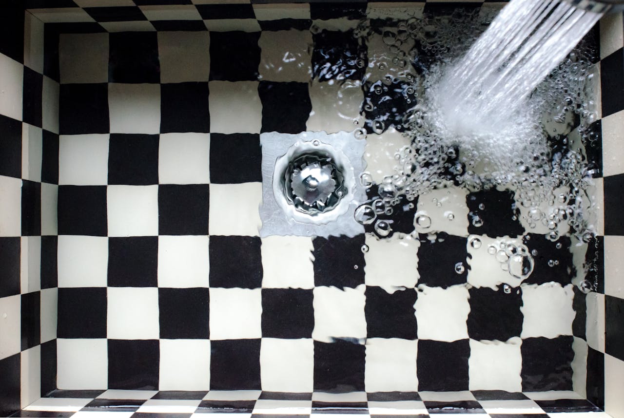 Water stream falling on checkered sink with metal drain
