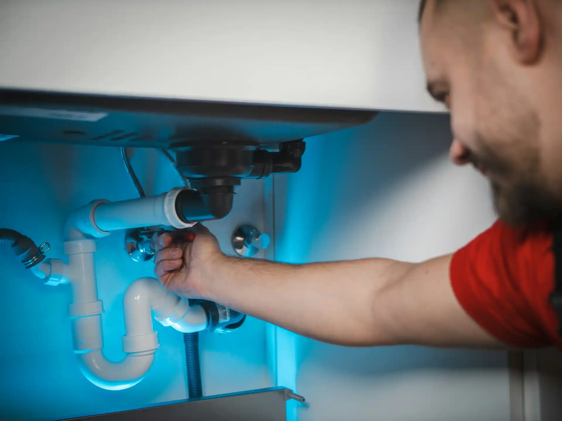Plumber fixing sink pipes under blue light in kitchen cabinet
