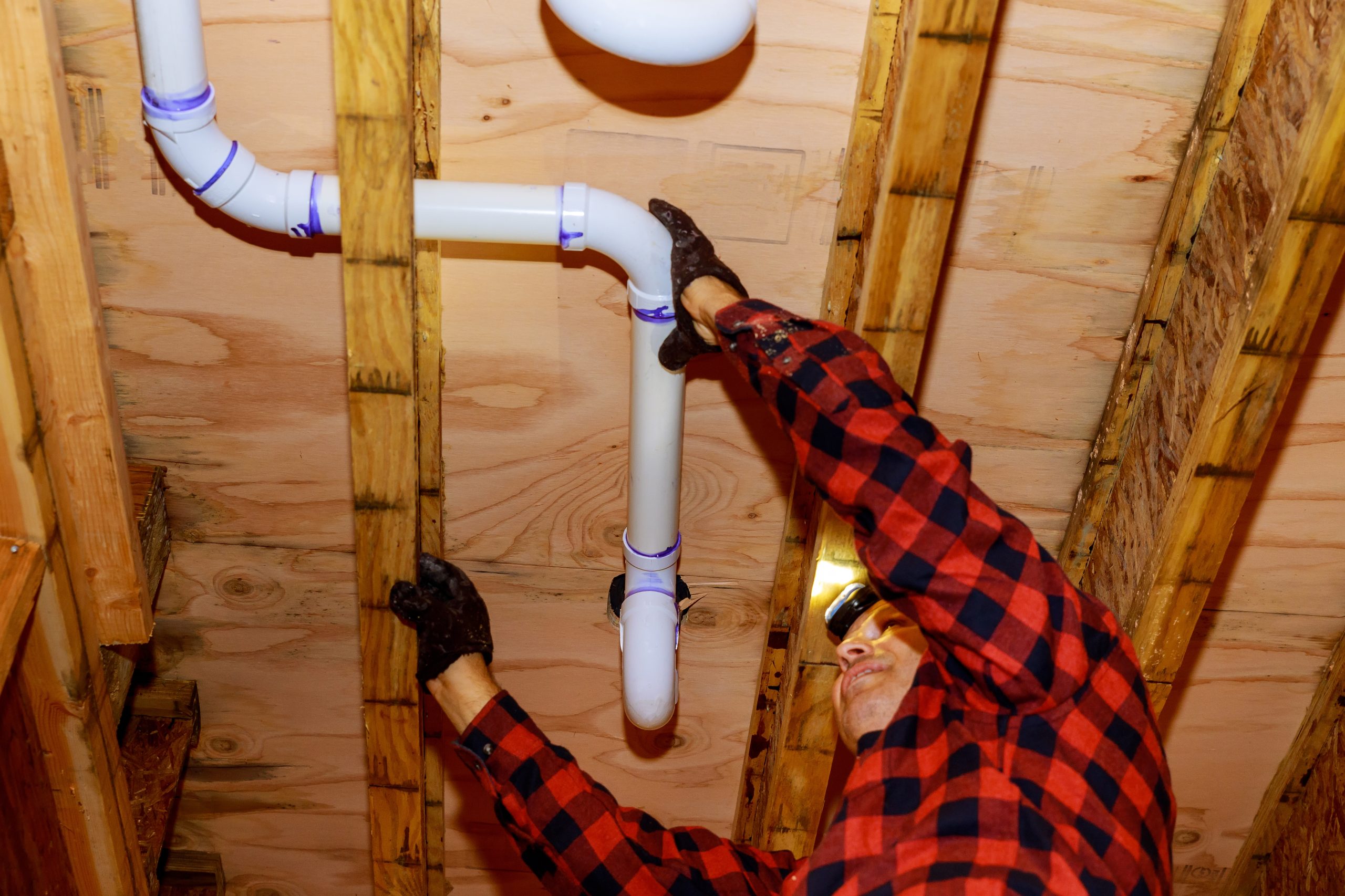 Plumber in red plaid shirt fixing pipes in wooden framed construction